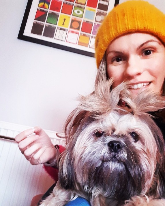 Picture of a woman in a winter woolly hat with a small dog. 
