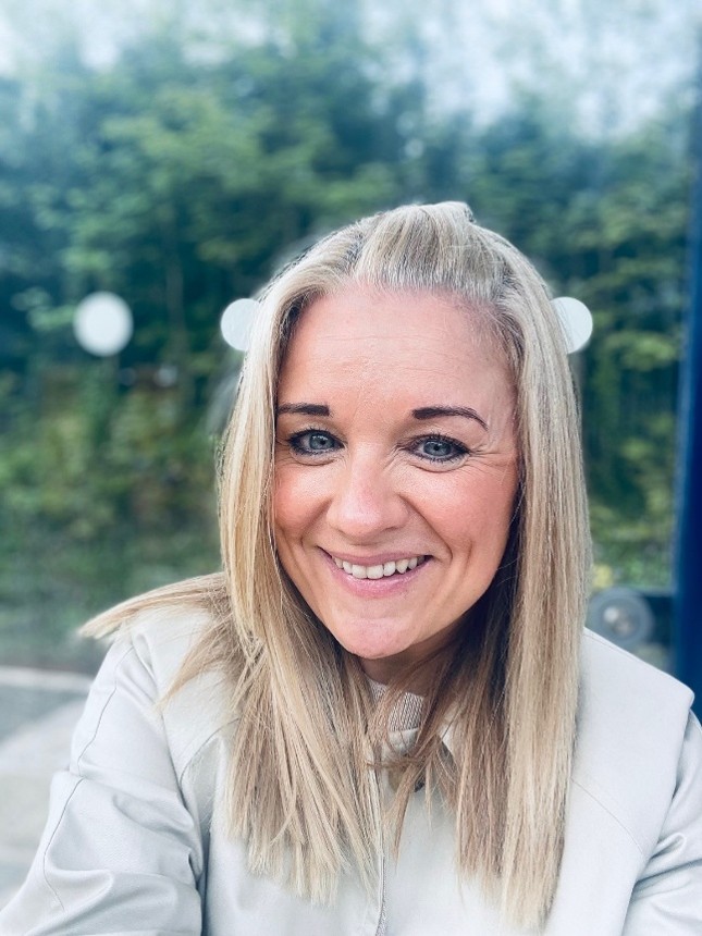 Headshot of a smiling woman with trees in the background.
