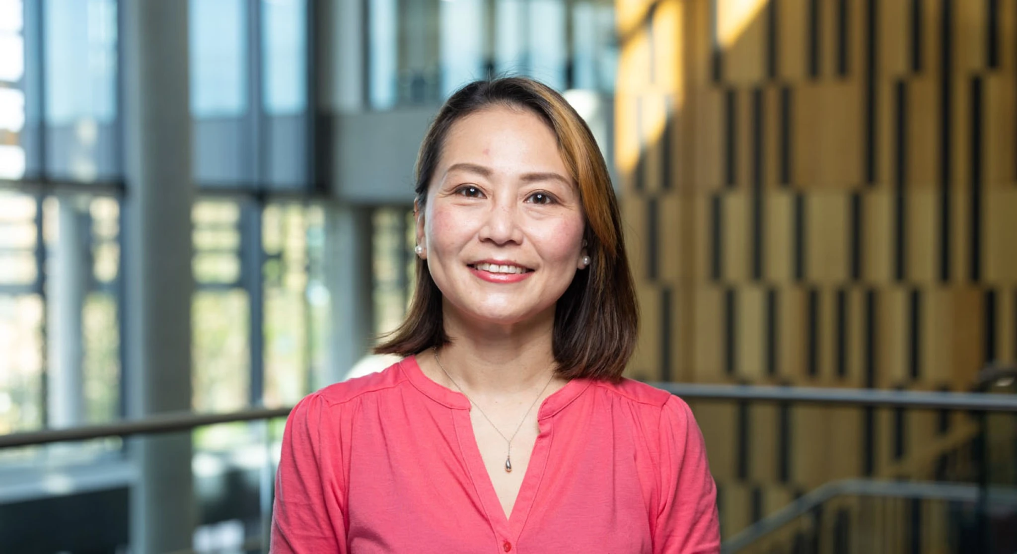 A professional headshot of a woman wearing a pink top. She is smiling.
